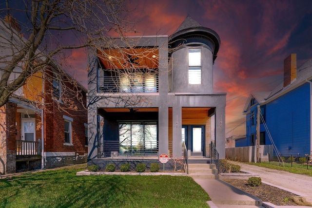 view of front of house featuring stucco siding, a porch, fence, a balcony, and a front lawn