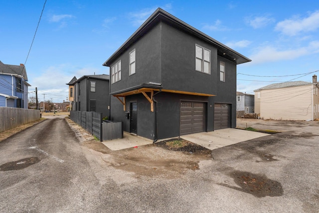 exterior space featuring a garage, driveway, fence, and stucco siding