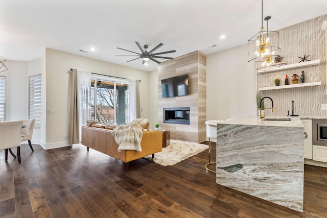 living area featuring a large fireplace, dark wood finished floors, a ceiling fan, and baseboards