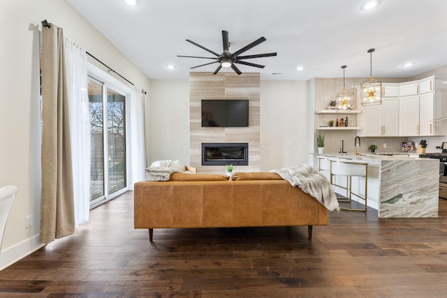 living room featuring a large fireplace, ceiling fan, dark wood-type flooring, and recessed lighting