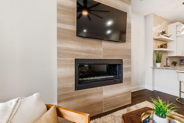 living room with a tile fireplace, dark wood finished floors, wet bar, and baseboards