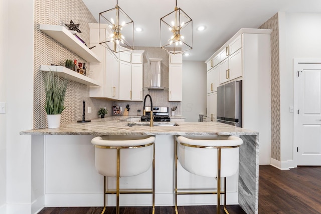 kitchen with appliances with stainless steel finishes, dark wood-type flooring, wall chimney range hood, light stone countertops, and a peninsula