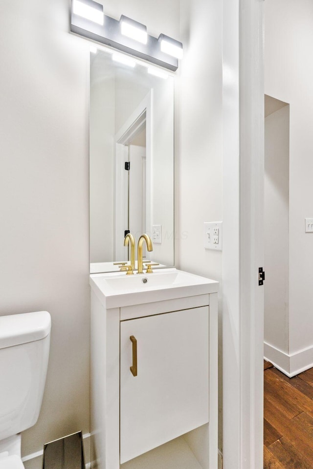 bathroom featuring toilet, baseboards, wood finished floors, and vanity