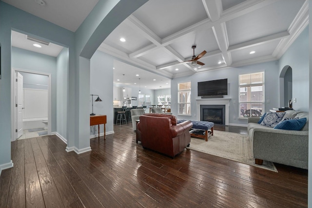 living area featuring a glass covered fireplace, beam ceiling, dark wood-style flooring, and coffered ceiling