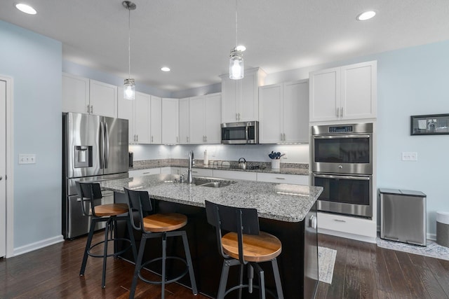 kitchen featuring light stone countertops, a center island with sink, dark wood finished floors, a sink, and stainless steel appliances