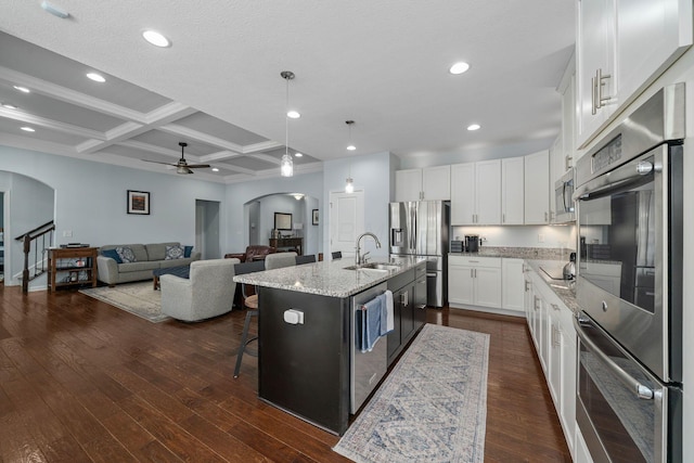 kitchen with a sink, stainless steel appliances, arched walkways, and dark wood-style flooring