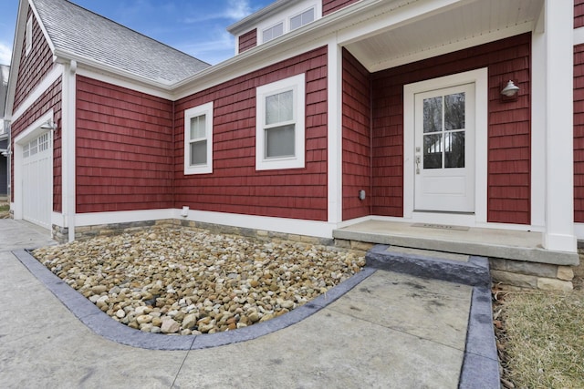 view of exterior entry featuring a garage and a shingled roof