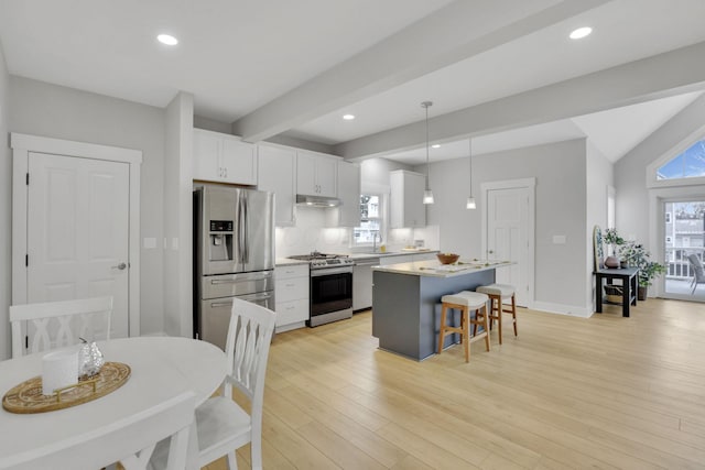 kitchen featuring appliances with stainless steel finishes, a breakfast bar, a center island, under cabinet range hood, and a sink