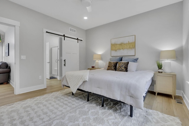 bedroom featuring a barn door, recessed lighting, visible vents, baseboards, and light wood finished floors