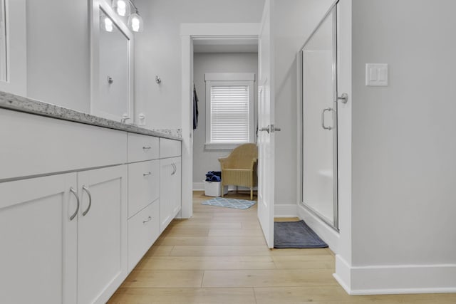 full bath featuring baseboards, wood finished floors, vanity, and a shower stall