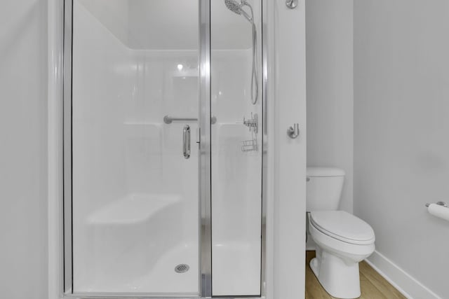 bathroom with toilet, a shower stall, baseboards, and wood finished floors