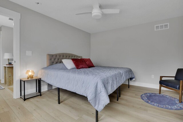 bedroom with a ceiling fan, wood finished floors, visible vents, and baseboards