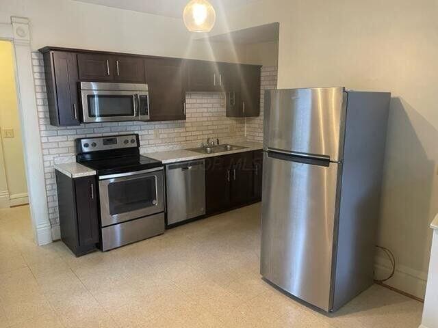 kitchen with a sink, light countertops, appliances with stainless steel finishes, light floors, and tasteful backsplash