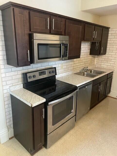 kitchen featuring appliances with stainless steel finishes, light countertops, a sink, and dark brown cabinets