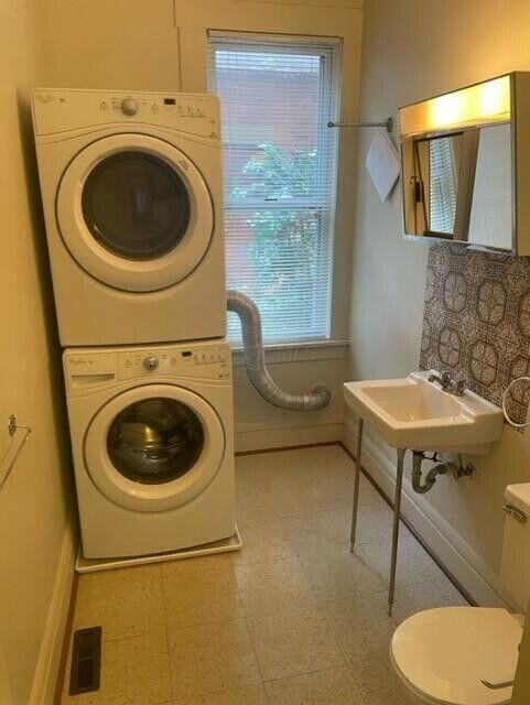 clothes washing area with baseboards, laundry area, visible vents, and stacked washer / drying machine