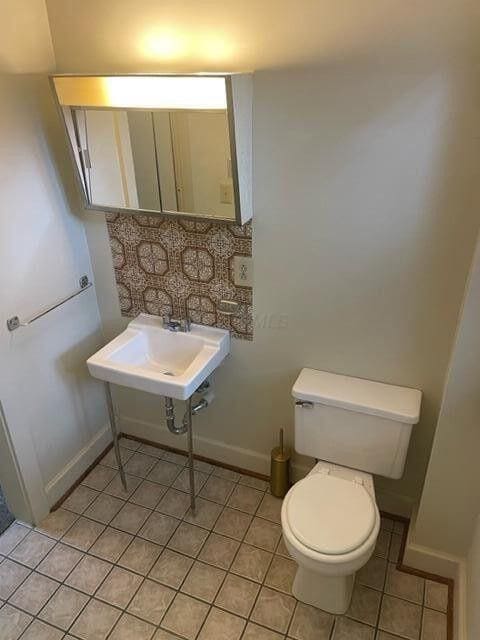 bathroom featuring toilet, tile patterned flooring, baseboards, and a sink