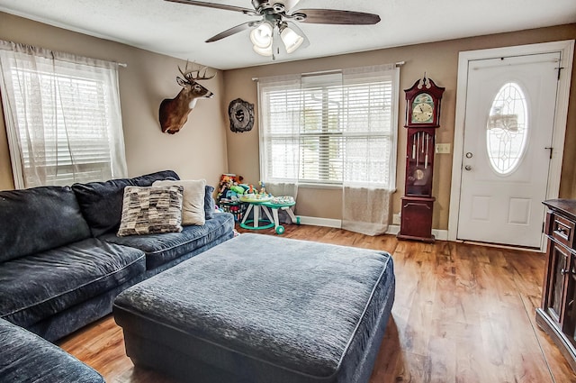 living area with baseboards, a ceiling fan, and light wood-style floors