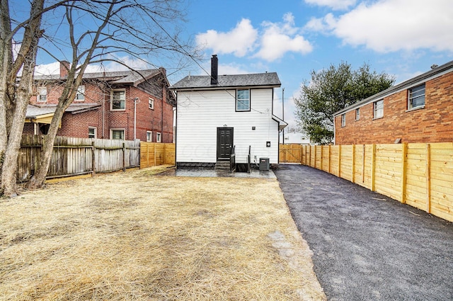 back of house with entry steps, a fenced backyard, a chimney, and central AC unit