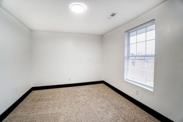 spare room featuring dark colored carpet, visible vents, and baseboards