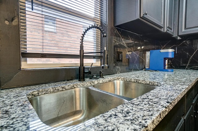 kitchen featuring light stone counters, gray cabinets, a sink, and decorative backsplash