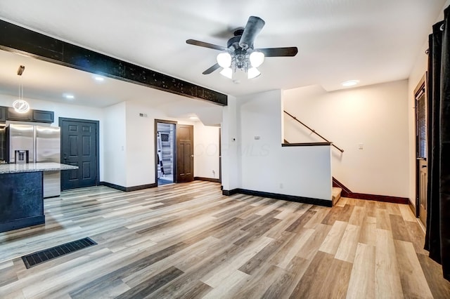 unfurnished living room featuring baseboards, visible vents, beamed ceiling, stairs, and light wood-type flooring