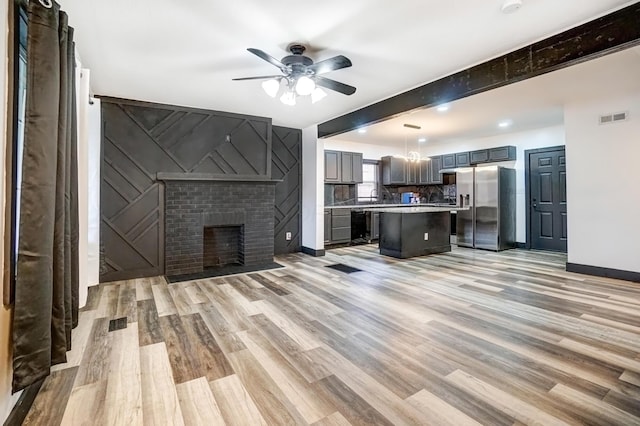 unfurnished living room with light wood-type flooring, baseboards, visible vents, and ceiling fan