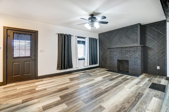 unfurnished living room featuring baseboards, ceiling fan, a fireplace, and light wood-style floors