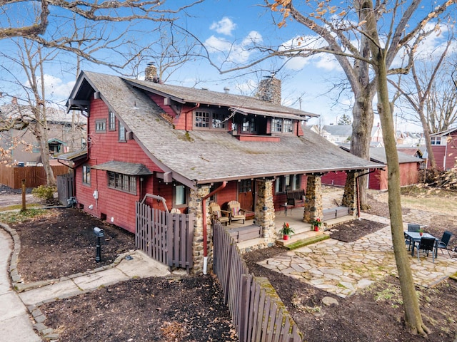 view of front of house featuring fence private yard, a chimney, a patio, and roof with shingles