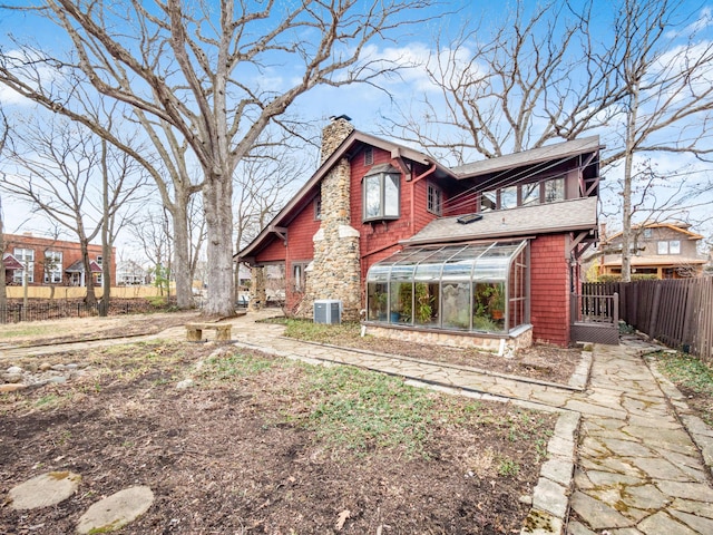 rear view of property with a sunroom, a chimney, fence, and central AC