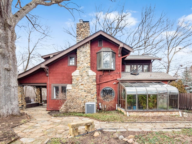 rear view of property featuring a shingled roof, a sunroom, a chimney, fence, and cooling unit