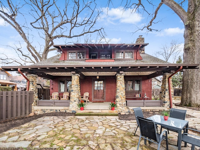 rear view of house with covered porch, roof with shingles, fence, and a chimney