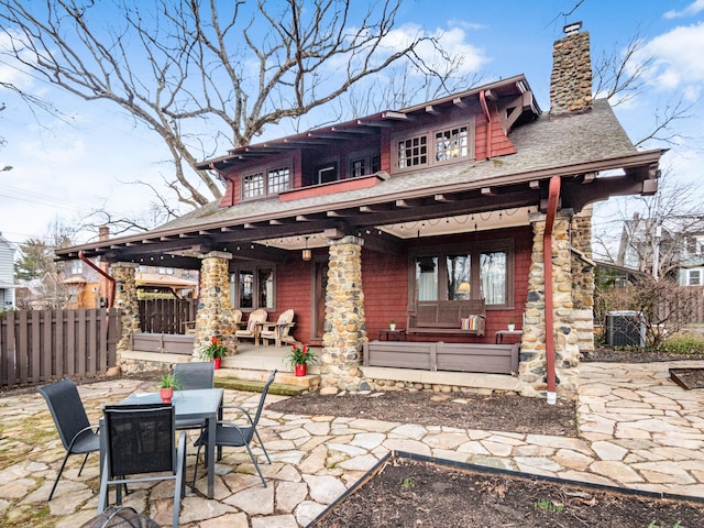 rear view of house with a patio, a shingled roof, fence, outdoor dining space, and a chimney