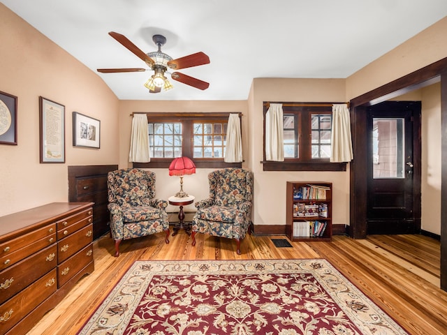 living area featuring lofted ceiling, light wood finished floors, a ceiling fan, and baseboards