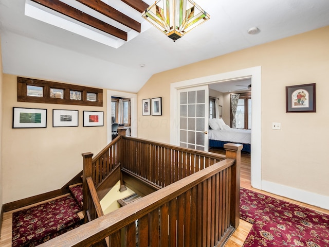 corridor with light wood-style floors, vaulted ceiling with skylight, baseboards, and an upstairs landing