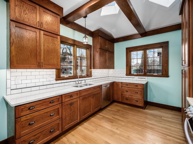 kitchen with a skylight, backsplash, stainless steel dishwasher, and a sink