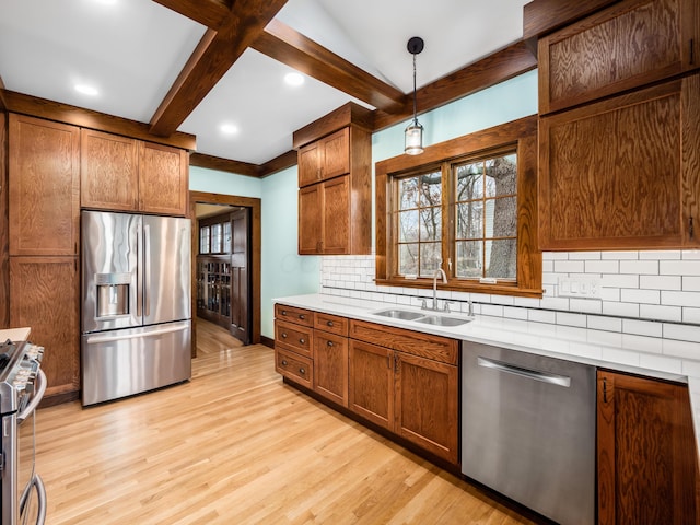 kitchen featuring brown cabinets, light wood-style flooring, appliances with stainless steel finishes, a sink, and beamed ceiling