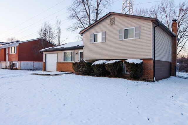 snow covered property featuring brick siding, a chimney, and an attached garage