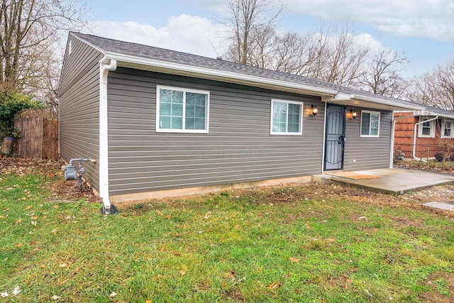 rear view of property featuring roof with shingles, a lawn, and fence