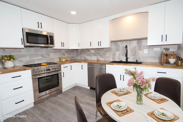 kitchen with light wood-style flooring, stainless steel appliances, a sink, wooden counters, and backsplash