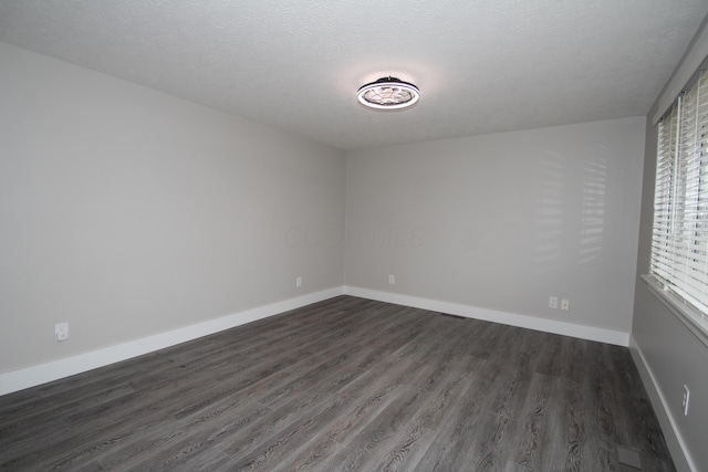 spare room with a textured ceiling, dark wood finished floors, and baseboards