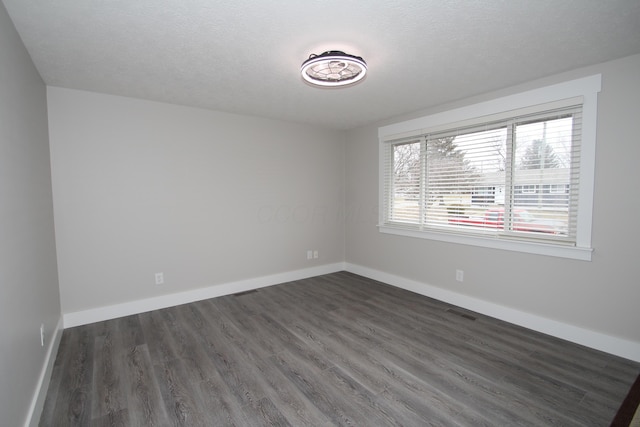 empty room featuring dark wood-style flooring, a textured ceiling, and baseboards