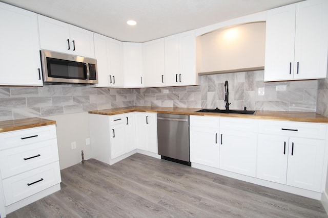 kitchen featuring backsplash, light wood-style flooring, appliances with stainless steel finishes, white cabinetry, and a sink