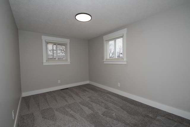 spare room featuring plenty of natural light, dark carpet, a textured ceiling, and baseboards