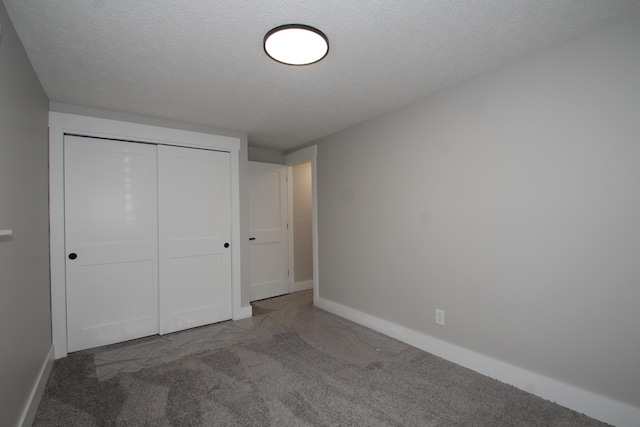 unfurnished bedroom with a textured ceiling, carpet floors, a closet, and baseboards