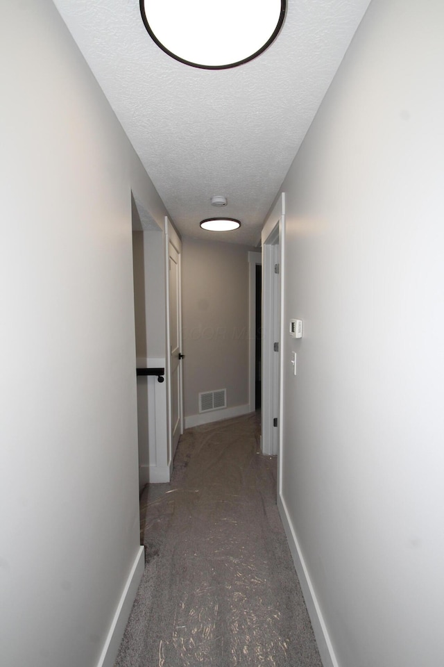 hallway with baseboards, visible vents, and a textured ceiling