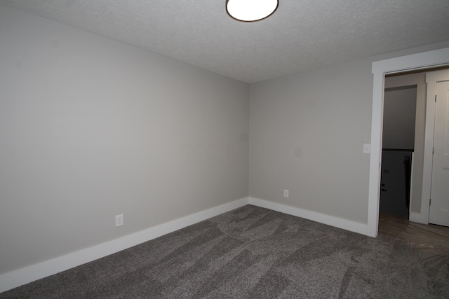 empty room with a textured ceiling, dark carpet, and baseboards