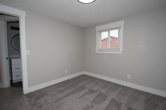 unfurnished bedroom with a textured ceiling, dark colored carpet, and baseboards