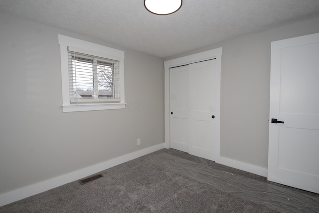 unfurnished bedroom featuring a textured ceiling, visible vents, baseboards, a closet, and dark carpet