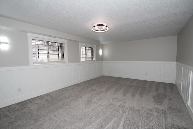 empty room with carpet, wainscoting, and a textured ceiling