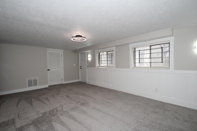 unfurnished room with visible vents, a textured ceiling, and carpet flooring